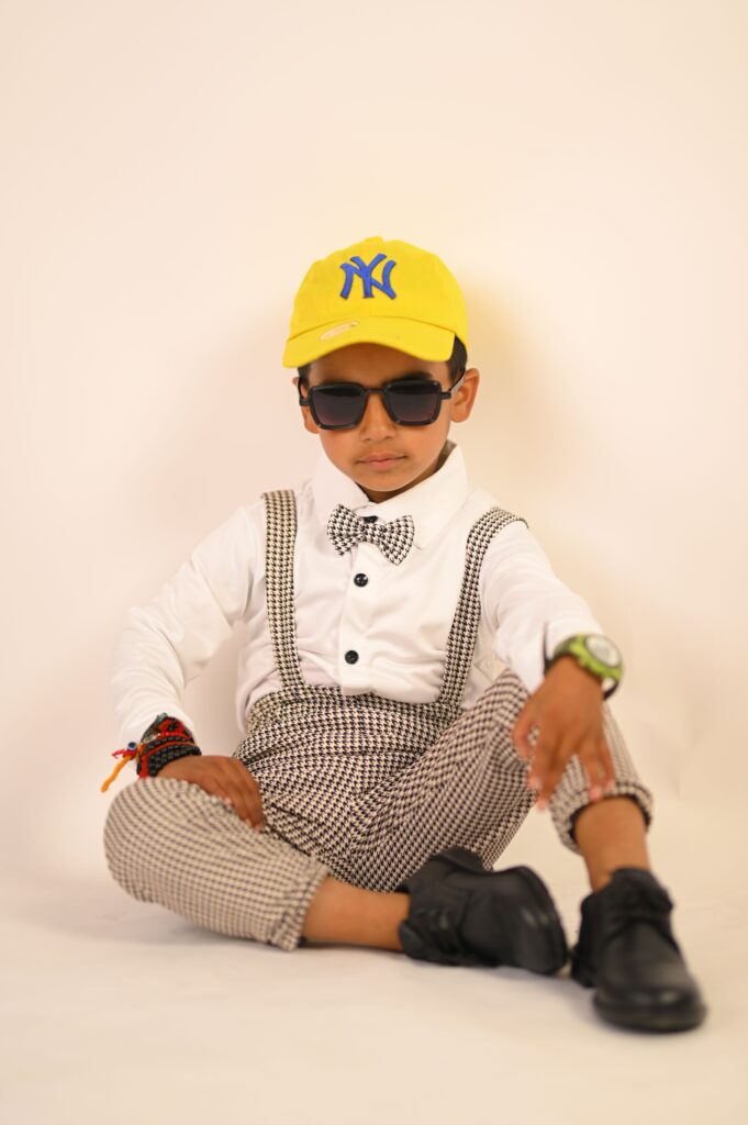 Fashionable young boy posing with sunglasses against a yellow background.